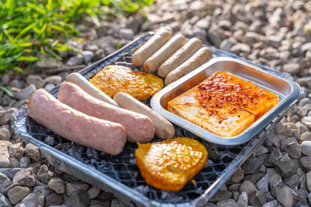 Bavaria, Germany - 2 September 2023: Vegetarian Grilling, Bratwurst Vegan and Vegetarian on a disposable grill on pebbles next to a meadow. Meat and sausage substitutes
