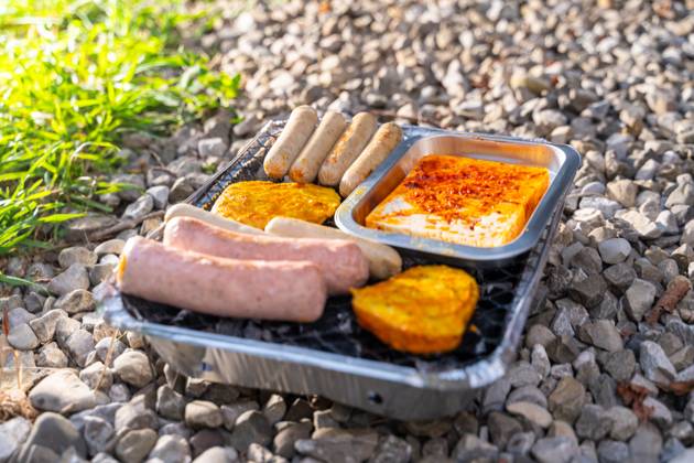 Bavaria, Germany - 2 September 2023: Vegetarian Grilling, Bratwurst Vegan and Vegetarian on a disposable grill on pebbles next to a meadow. Meat and sausage substitutes