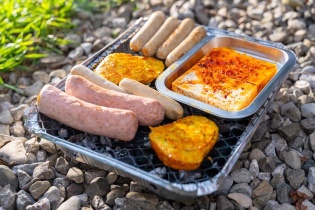 Bavaria, Germany - 2 September 2023: Vegetarian Grilling, Bratwurst Vegan and Vegetarian on a disposable grill on pebbles next to a meadow. Meat and sausage substitutes
