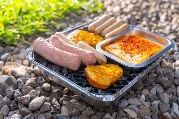 Bavaria, Germany - 2 September 2023: Vegetarian Grilling, Bratwurst Vegan and Vegetarian on a disposable grill on pebbles next to a meadow. Meat and sausage substitutes