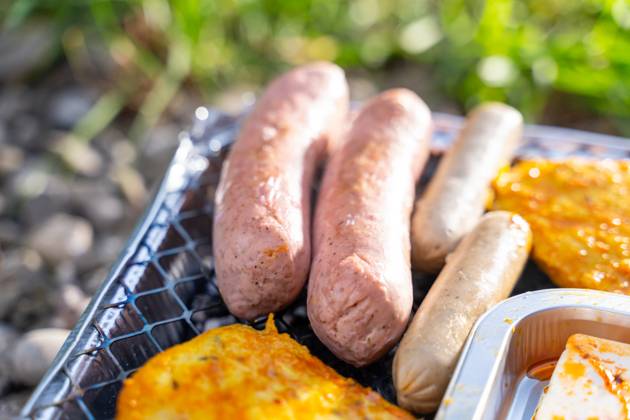 Bavaria, Germany - 2 September 2023: Vegetarian Grilling, Bratwurst Vegan and Vegetarian on a disposable grill on pebbles next to a meadow. Meat and sausage substitutes
