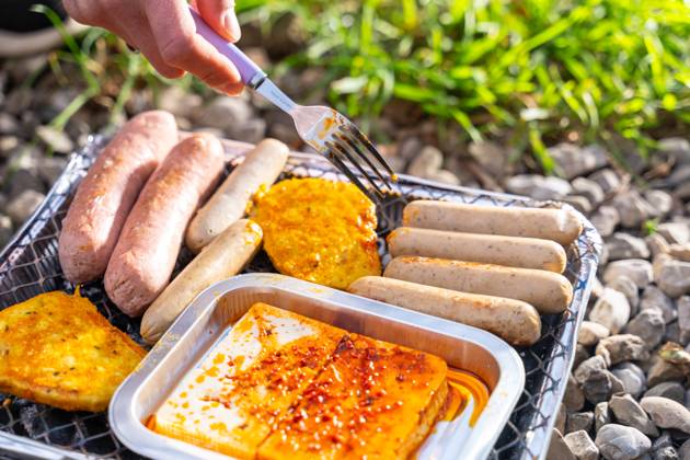 Bavaria, Germany - 2 September 2023: Vegetarian Grilling, Bratwurst Vegan and Vegetarian on a disposable grill. Meat and sausage substitutes. Hand turns grilled food with a fork