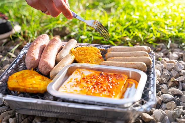 Bavaria, Germany - 2 September 2023: Vegetarian Grilling, Bratwurst Vegan and Vegetarian on a disposable grill. Meat and sausage substitutes. Hand turns grilled food with a fork