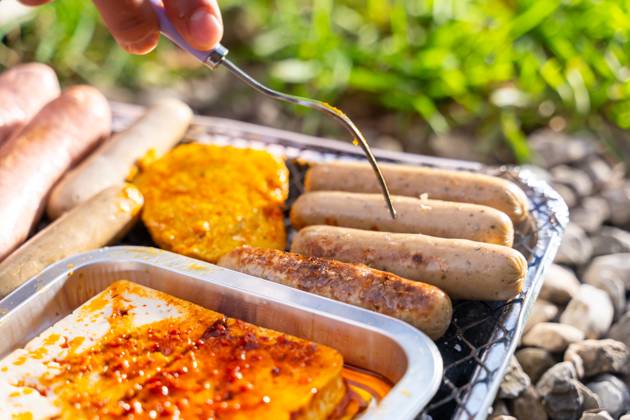 Bavaria, Germany - 2 September 2023: Vegetarian Grilling, Bratwurst Vegan and Vegetarian on a disposable grill. Meat and sausage substitutes. Hand turns grilled food with a fork