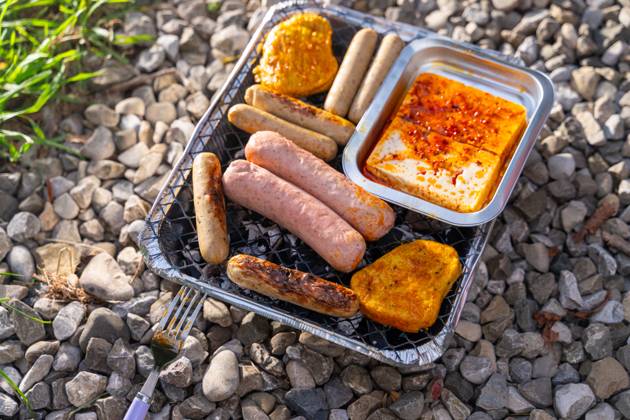 Bavaria, Germany - 2 September 2023: Vegetarian Grilling, Bratwurst Vegan and Vegetarian on a disposable grill on pebbles next to a meadow. Meat and sausage substitutes