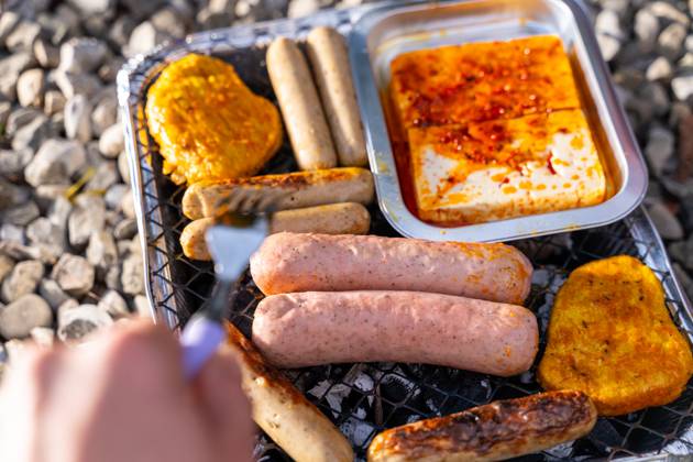 Bavaria, Germany - 2 September 2023: Vegetarian Grilling, Bratwurst Vegan and Vegetarian on a disposable grill. Meat and sausage substitutes. Hand turns grilled food with a fork