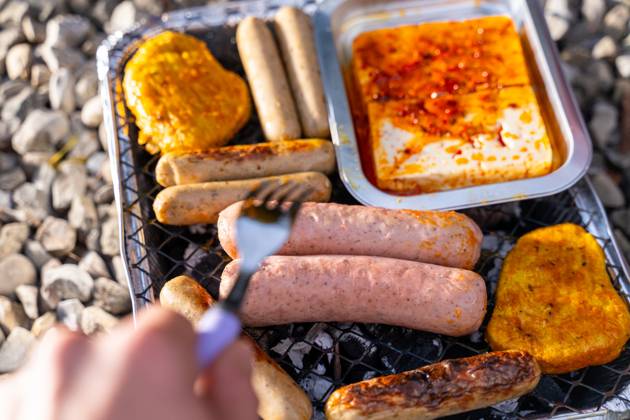 Bavaria, Germany - 2 September 2023: Vegetarian Grilling, Bratwurst Vegan and Vegetarian on a disposable grill. Meat and sausage substitutes. Hand turns grilled food with a fork