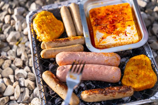 Bavaria, Germany - 2 September 2023: Vegetarian Grilling, Bratwurst Vegan and Vegetarian on a disposable grill. Meat and sausage substitutes. Hand turns grilled food with a fork