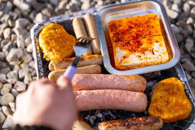 Bavaria, Germany - 2 September 2023: Vegetarian Grilling, Bratwurst Vegan and Vegetarian on a disposable grill. Meat and sausage substitutes. Hand turns grilled food with a fork