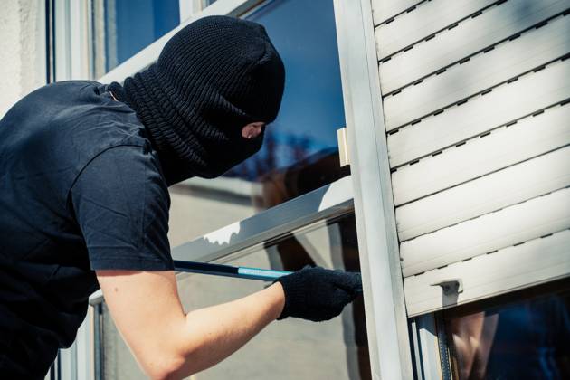 Augsburg, Bavaria, Germany - August 7, 2023: Symbol image burglary in the apartment, apartment burglary. Masked burglar levering open the door from a terrace of a house with a crowbar