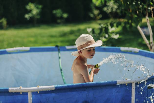 Boy wearing hat playing with water pipe in wading pool on sunny day model released, Symbolfoto, VSNF01330