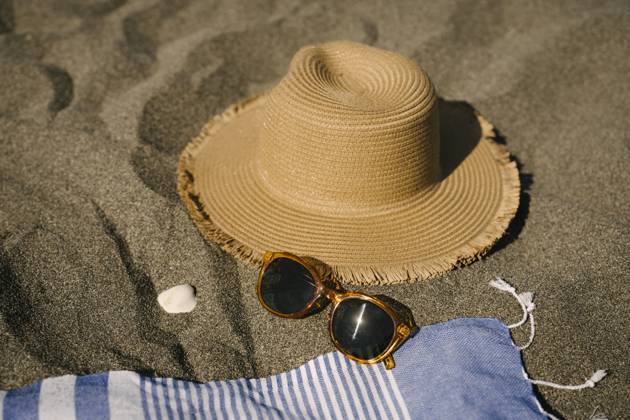 Sun hat next to sunglasses on sand at beach, YBF00201