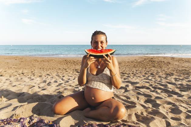 Pregnant woman sitting on sand and eating watermelon at beach model released, Symbolfoto, PCLF00714