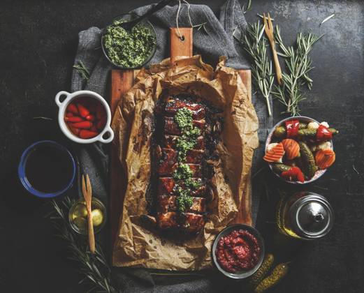 Roasted BBQ ribs with homemade pesto, pickled vegetables, sauces and rosemary on dark concrete kitchen table. Flavorful seasoned meat for dinner. Top view. Model Released Vicuschka_ID16617_505418_009 Copyright: xx