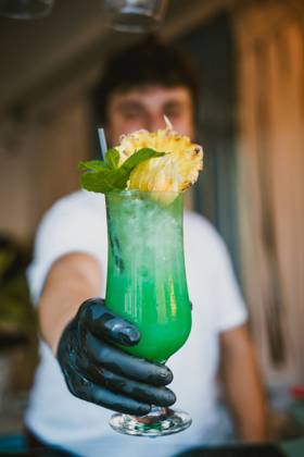 Blurred young male bartender showing a tropical green cocktail with a pineapple garnish at a bar Model Released AlvaroMontero_ID17423_529018_002 Copyright: xAlvaroxMonterox RECORD DATE NOT STATED