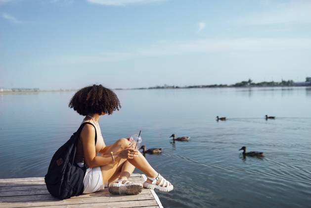 Beautiful mixed race female teenager sits on wooden pier and drinks cocktail in plactic glass. Charming african girl in casual clothes and with black backpack smiles sincerely near water. Sunny day. Beautiful mixed race female teenager sits on wooden pier and drinks cocktail in plactic glass. Charming african girl in casual clothes and with black backpack smiles sincerely near water. Sunny day. ,model released, Symbolfoto Copyright: xZoonar.com DashaxPetrenkox 20707055 ,model released, Symbolfoto ,property released