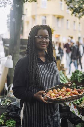 IMAGO Creative, Jahreszeit Sommer, Food, Pflaume Portrait of smiling female vendor holding tray of fresh plums while standing at farmer s market Sweden, Stockholm, model released Copyright: xMaskotx , MA105823 MA105823