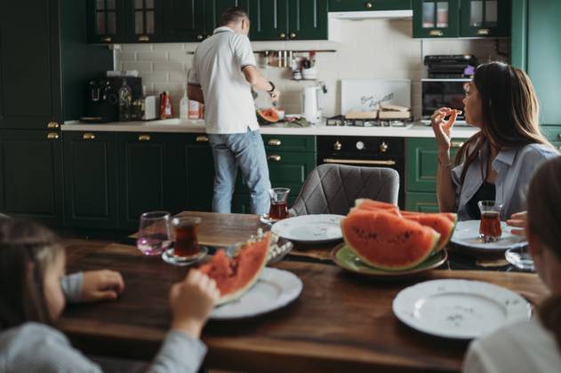 Mother and daughters having lunch at table with man cutting watermelon in kitchen model released, Symbolfoto property released, ANAF02423