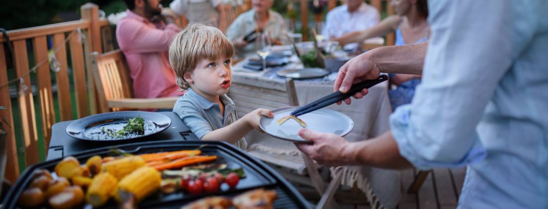 Father putting grilled meat and vegetable on plate to his son during family summer garden party. A father putting grilled meat and vegetable on plate to his son during family summer garden party. model released Copyright: xx HHH FAMILY GRILL BODOVCI 2022 HHH 129