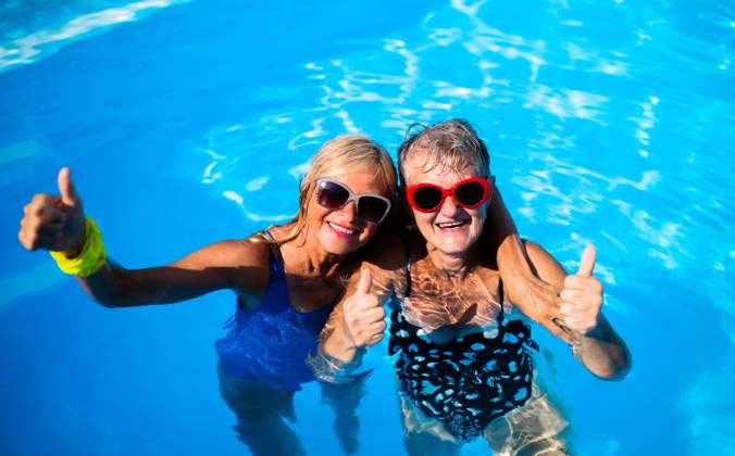 High angle view of cheerful senior women in swimming pool outdoors in backyard. High angle view of cheerful senior women in swimming pool outdoors in backyard, looking at camera. model released Copyright: xx Summer_Splash_Seniors_2020_315