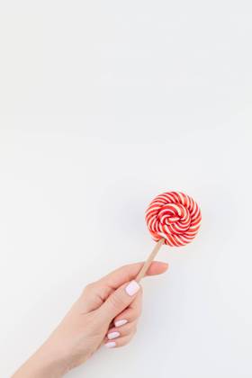 Woman hand with red lollipop Woman hand with pastel manicure polish holding bright red swirling lollipop isolated on white background copy space minimalism style. Template for feminine social media. Fun and celebration concept Copyright: xZoonar.com AnastasiaxZolotnitskayax 20824271