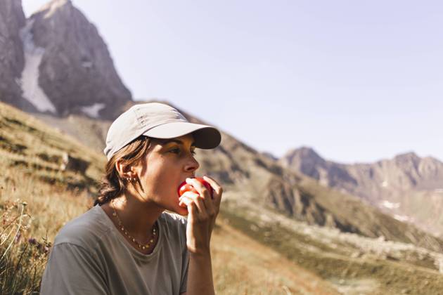 Woman wearing cap and eating tomato in front of mountains on sunny day model released, Symbolfoto, PCLF00956