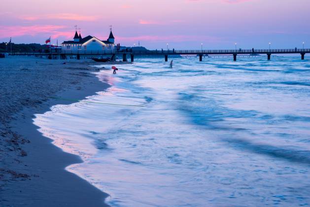 quiet Abendstimmung on Beach with quiet Waves and Two Person near a Seabridge with Building in the Dusk, clearer, Blue purple Sky with Pink Clouds, Seabridge Ahlbeck at last Evening light, Motion blur, Wiping effect, Long exposure, View from Western Beach, Seaside resort Ahlbeck, Island Usedom, Mecklenburg Western Pomerania, Germany, Europe Copyright: imageBROKER/CarolaxVahldiek ibxcva10113590.jpg