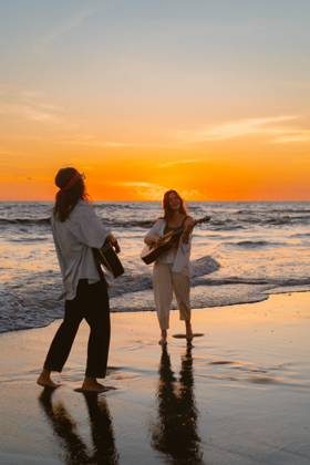IMAGO Creative, Jahreszeit Sommer, Sommerferien Women friends play guitars on the beach. Sunset on the ocean. Bali Kuta, Bali, Indonesia CR_YUKI240206-1331712-01 ,model released, Symbolfoto ,property released