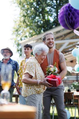 Garden birthday party for senior lady. Beautiful senior birthday woman receiving birthday gift from grandson. Garden birthday party for senior lady. Beautiful senior birthday woman receiving birthday wishes and gifts from grandson. model released
