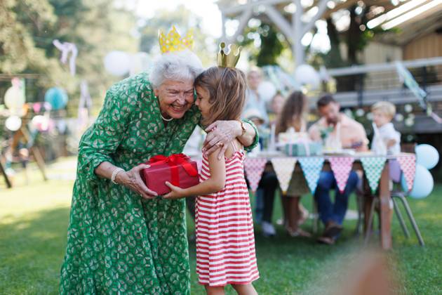 Garden birthday party for senior lady. Beautiful senior birthday woman receiving gift from granddaughter. Garden birthday party for senior lady. Beautiful senior birthday woman receiving gift from granddaughter, hugging. model released