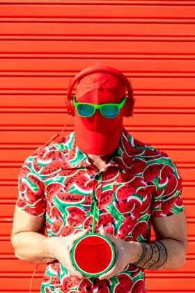 Anonymous man in printed shirt covering face with hat Unrecognizable street style male with hat covering face and wearing sunglasses headphones in place while standing in printed water melon slices shirt and carrying mock juice against red background Model Released SergioVictorVega_ID19622_581839_004 Copyright: xSergioxVictorxVegax RECORD DATE NOT STATED