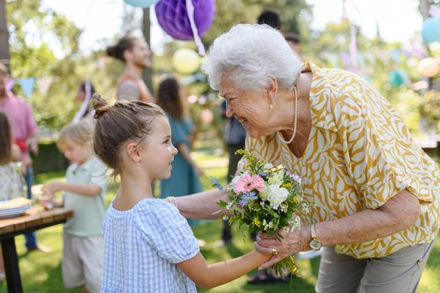 Garden birthday party for senior lady. Beautiful senior birthday woman receiving gift from granddaughter. Garden birthday party for senior lady. Beautiful senior birthday woman receiving gift from granddaughter, hugging. model released