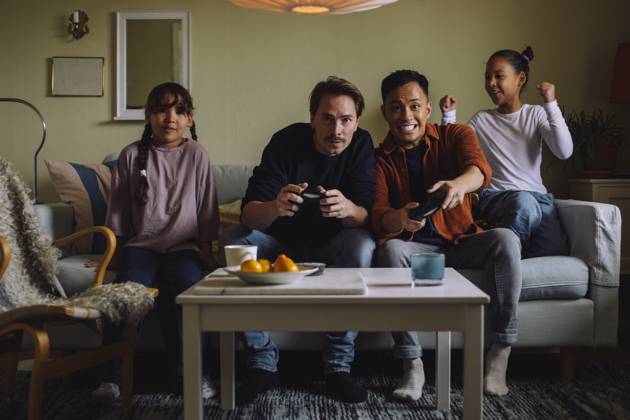 IMAGO Creative, Lifestyle, Gaming Excited gay couple competing while playing video game with daughter sitting on sofa at home Sweden, Stockholm, model released, property released Copyright: xMaskotx , MA107533 MA107533