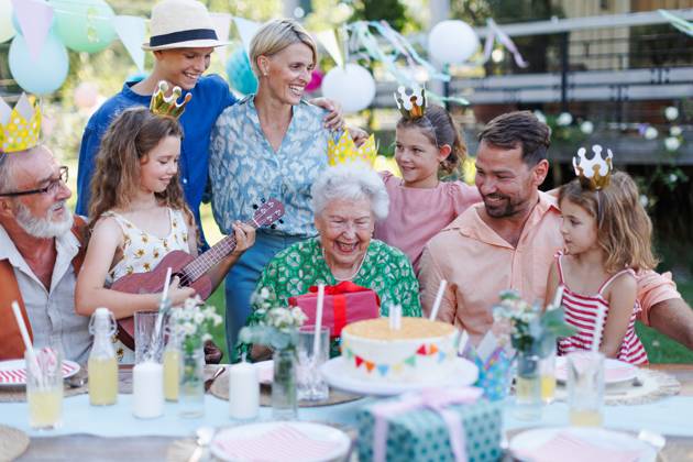 Garden birthday party for senior lady. Beautiful senior birthday woman receiving gift from family. Garden birthday party for senior lady. Beautiful senior birthday woman receiving gift from granddaughter, family and friends. Birthday celebration with paper crowns. model released