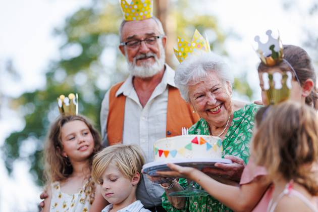 Garden birthday party for senior lady. Beautiful senior birthday woman receiving gift from family. Garden birthday party for senior lady. Beautiful senior birthday woman receiving gift from granddaughter, family and friends. Birthday celebration with paper crowns. model released