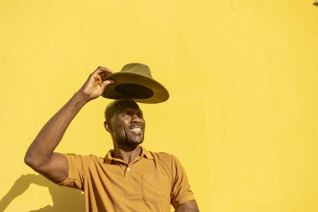 A cheerful African man tipping his hat with a sunny yellow background, evoking warmth and happiness Model Released JuanAizpuru_ID20348_601907_036 Copyright: xJuanxAizpurux