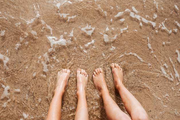 Close up of feet on beach with sea water beneath them. Sea foam and warm water soaking legs. Close up of feet on beach with sea water beneath. Sea foam and warm water soaking legs. model released