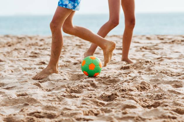 Siblings playing on beach with ball, playing football. Concept of family beach summer vacation with kids. Siblings playing on beach with ball, playing football. Concept of family beach summer vacation with kids. Close up on legs. model released