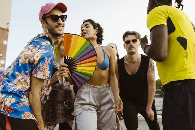 Non-binary person holding hand fan and dancing with multiracial friends in city Germany, Berlin, model released Copyright: xMaskotx , MA108332 MA108332
