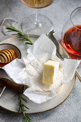 An elegant presentation of brie cheese with honeycomb, rosemary, and wine glasses on a textured surface for sophisticated dining. Model Released AnnaBogush_ID20594_608291_009 Copyright: xAnnaxBogushx