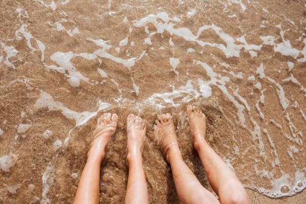 Close up of feet on beach with sea water beneath them. Sea foam and warm water soaking legs. Close up of feet on beach with sea water beneath. Sea foam and warm water soaking legs. model released