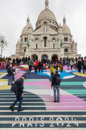 Paris, France April 19, 2024 - People walk up the stairs leading to the Sacre Coeur basilica decorated with a fresco in Olympic colors as part of the preparations for the Paris 2024 Olympic Games. Less than 100 days remain for the Olympic and Paralympic Games organizers to finalize preparations for the event that will welcome millions of visitors from July 16. OLY, JEUX OLYMPIQUES PARIS 2024, DECORATIONS, FRESQUE, ILLUSTRATION, MONTMARTRE, BASILIQUE DU SACRE COEUR, SPORT, ESCALIERS, MARCHES COLOREES, Copyright: xVincentxIsorex