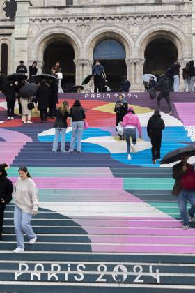 Paris, France April 19, 2024 - People walk up the stairs leading to the Sacre Coeur basilica decorated with a fresco in Olympic colors as part of the preparations for the Paris 2024 Olympic Games. Less than 100 days remain for the Olympic and Paralympic Games organizers to finalize preparations for the event that will welcome millions of visitors from July 16. OLY, JEUX OLYMPIQUES PARIS 2024, DECORATIONS, FRESQUE, ILLUSTRATION, MONTMARTRE, BASILIQUE DU SACRE COEUR, SPORT, ESCALIERS, MARCHES COLOREES, Copyright: xVincentxIsorex
