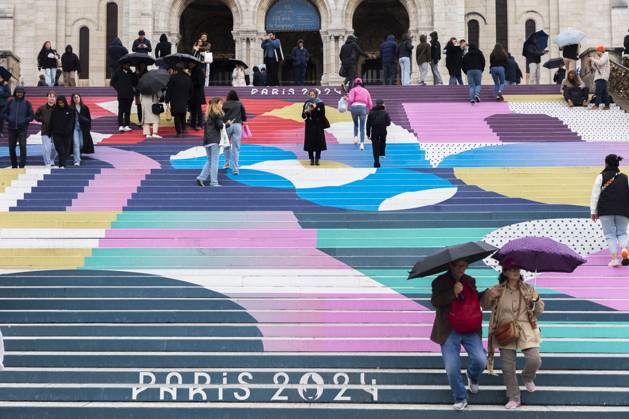 Paris, France April 19, 2024 - People walk up the stairs leading to the Sacre Coeur basilica decorated with a fresco in Olympic colors as part of the preparations for the Paris 2024 Olympic Games. Less than 100 days remain for the Olympic and Paralympic Games organizers to finalize preparations for the event that will welcome millions of visitors from July 16. OLY, JEUX OLYMPIQUES PARIS 2024, DECORATIONS, FRESQUE, ILLUSTRATION, MONTMARTRE, BASILIQUE DU SACRE COEUR, SPORT, ESCALIERS, MARCHES COLOREES, Copyright: xVincentxIsorex