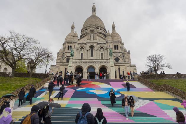 Paris, France April 19, 2024 - People walk up the stairs leading to the Sacre Coeur basilica decorated with a fresco in Olympic colors as part of the preparations for the Paris 2024 Olympic Games. Less than 100 days remain for the Olympic and Paralympic Games organizers to finalize preparations for the event that will welcome millions of visitors from July 16. OLY, JEUX OLYMPIQUES PARIS 2024, DECORATIONS, FRESQUE, ILLUSTRATION, MONTMARTRE, BASILIQUE DU SACRE COEUR, SPORT, ESCALIERS, MARCHES COLOREES, Copyright: xVincentxIsorex