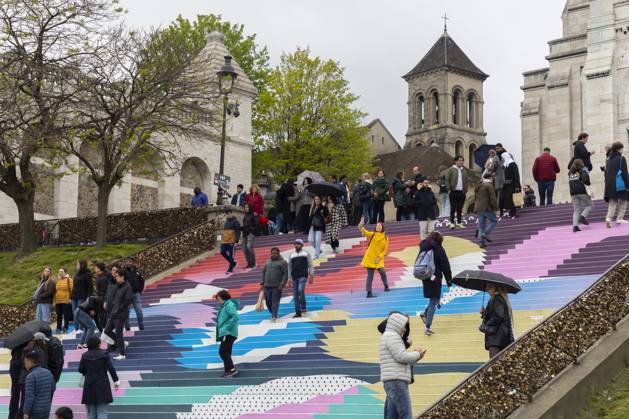 Paris, France April 19, 2024 - People walk up the stairs leading to the Sacre Coeur basilica decorated with a fresco in Olympic colors as part of the preparations for the Paris 2024 Olympic Games. Less than 100 days remain for the Olympic and Paralympic Games organizers to finalize preparations for the event that will welcome millions of visitors from July 16. OLY, JEUX OLYMPIQUES PARIS 2024, DECORATIONS, FRESQUE, ILLUSTRATION, MONTMARTRE, BASILIQUE DU SACRE COEUR, SPORT, ESCALIERS, MARCHES COLOREES, Copyright: xVincentxIsorex