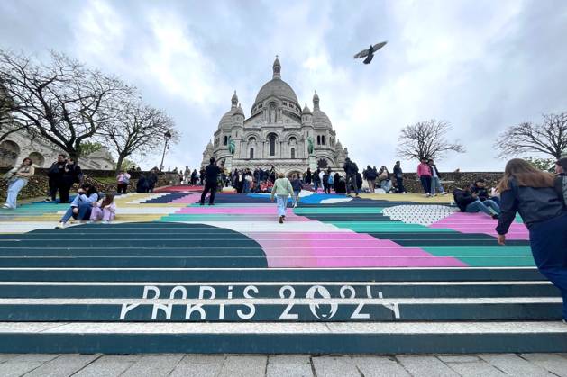 Paris, France April 19, 2024 - People walk up the stairs leading to the Sacre Coeur basilica decorated with a fresco in Olympic colors as part of the preparations for the Paris 2024 Olympic Games. Less than 100 days remain for the Olympic and Paralympic Games organizers to finalize preparations for the event that will welcome millions of visitors from July 16. OLY, JEUX OLYMPIQUES PARIS 2024, DECORATIONS, FRESQUE, ILLUSTRATION, MONTMARTRE, BASILIQUE DU SACRE COEUR, SPORT, ESCALIERS, MARCHES COLOREES, Copyright: xVincentxIsorex