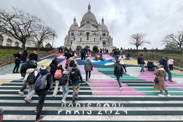 Paris, France April 19, 2024 - People walk up the stairs leading to the Sacre Coeur basilica decorated with a fresco in Olympic colors as part of the preparations for the Paris 2024 Olympic Games. Less than 100 days remain for the Olympic and Paralympic Games organizers to finalize preparations for the event that will welcome millions of visitors from July 16. OLY, JEUX OLYMPIQUES PARIS 2024, DECORATIONS, FRESQUE, ILLUSTRATION, MONTMARTRE, BASILIQUE DU SACRE COEUR, SPORT, ESCALIERS, MARCHES COLOREES, Copyright: xVincentxIsorex