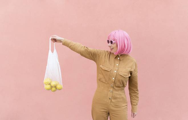 Smiling woman holding mesh bag with lemons in front of pink wall model released, Symbolfoto, VRAF00503