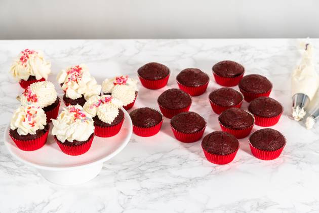 White chocolate ganache frosting Piping white chocolate ganache frosting on top of red velvet cupcakes and topping with sprinkles. Copyright: xArinaxHabich RECORD DATE NOT STATED